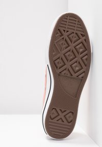 Semelle d'une chaussure Converse All Star rose montrant un motif de bande de roulement marron et des marquages de taille 43 sur fond blanc.