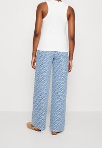 Top bianco senza maniche abbinato a pantaloni larghi blu con motivo a geometrie e texture morbida.