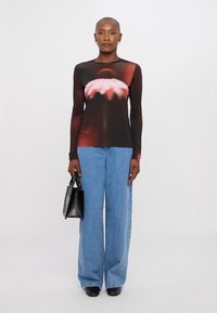 Maglietta nera a manica lunga con stampa floreale, abbinata a jeans in denim blu a gamba larga. La modella tiene in mano una piccola borsa nera.