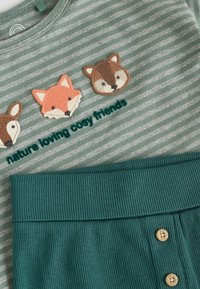 Grüner gestreifter Oberteil mit drei Tier-Patches (Fuchs, Reh, Dachs) und dem Text "Natur liebende kuschelige Freunde". Mit geripptem türkisfarbenem Bund und Knöpfen.