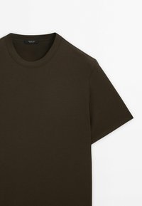 T-shirt di cotone marrone scuro con scollatura rotonda e maniche corte. Texture liscia con dettagli di cucitura minimi.