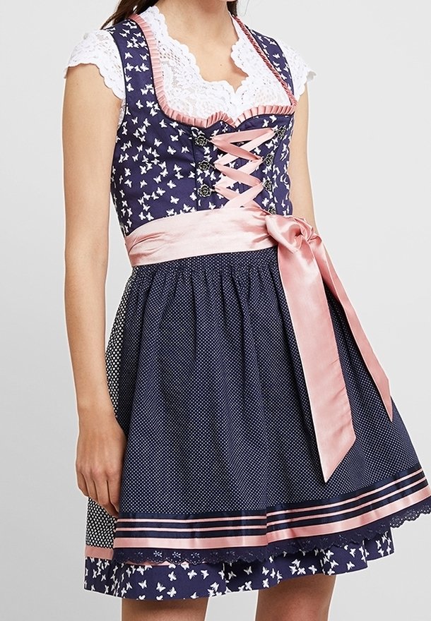 Kobieta w granatowej sukience dirndl w kwiaty, z białą koronkową bluzką i różową satynową wstążką zawiązaną w talii.