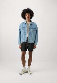 Light blue denim jacket with button closure, gray t-shirt, black shorts, and beige sneakers. Minimalist design, featuring contrasting textures.