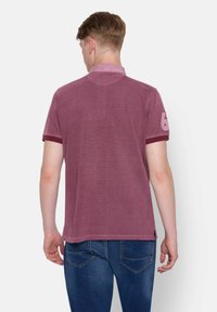 Burgundowa koszulka polo z krótkim rękawem, kołnierzykiem i małym numerem 6 wyszytym na lewym rękawie, wykonana z fakturowanej tkaniny.