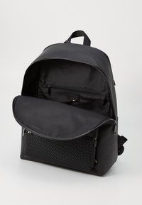 Black backpack featuring a structured design, smooth texture, front zippered pocket, and logo detail inside the spacious main compartment.
