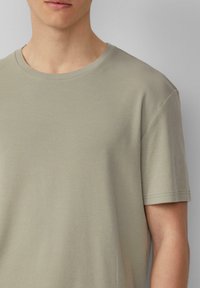 Jasno oliwkowa, prążkowana koszulka z okrągłym dekoltem, krótkimi rękawami i gładką, miękką teksturą. Posiada bezszwowe wykończenie przy dekolcie.