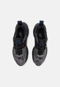 Černé a šedé sportovní boty s texturovanou tkaninou, elastickými šňůrkami, kontrastními námořnickými akcenty a poutkem na patě. Viditelné logo Nike.