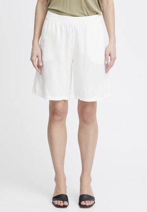 White linen shorts with an elastic waistband, featuring a loose fit and mid-thigh length, paired with black slide sandals.