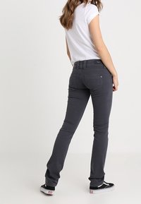 Grå denimjeans med slim fit, bakfickor och medelhögt midjeband, i kombination med svarta sneakers och en vit t-shirt.