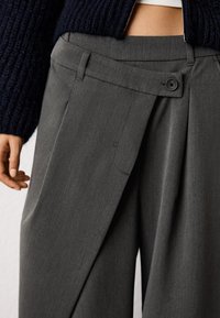 Gray tailored trousers with a pleated front, featuring a single button closure and side pockets, made of a smooth, textured fabric.
