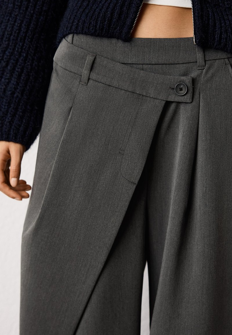 Gray tailored trousers with a pleated front, featuring a single button closure and side pockets, made of a smooth, textured fabric.
