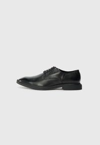 Zwarte leren dress shoe met een gladde textuur, spitse neus, zes veterogen vetersluiting en een lage rechthoekige hak. Subtiele merkopdruk aan de zijkant.