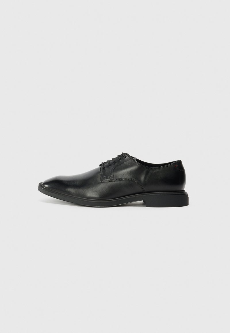 Zwarte leren dress shoe met een gladde textuur, spitse neus, zes veterogen vetersluiting en een lage rechthoekige hak. Subtiele merkopdruk aan de zijkant.