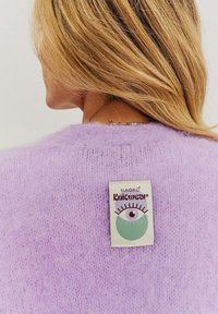 Lila pletený sveter z chlpatého materiálu, na zadnej strane so štítkom s grafikou oka a nápisom "Naoko Knitwear".