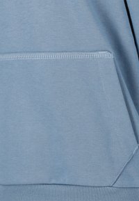 Lichtblauwe sweatshirtstof met een voorzak, ribbelboord en zichtbare stikdetails. Glad textuur met een casual ontwerp.
