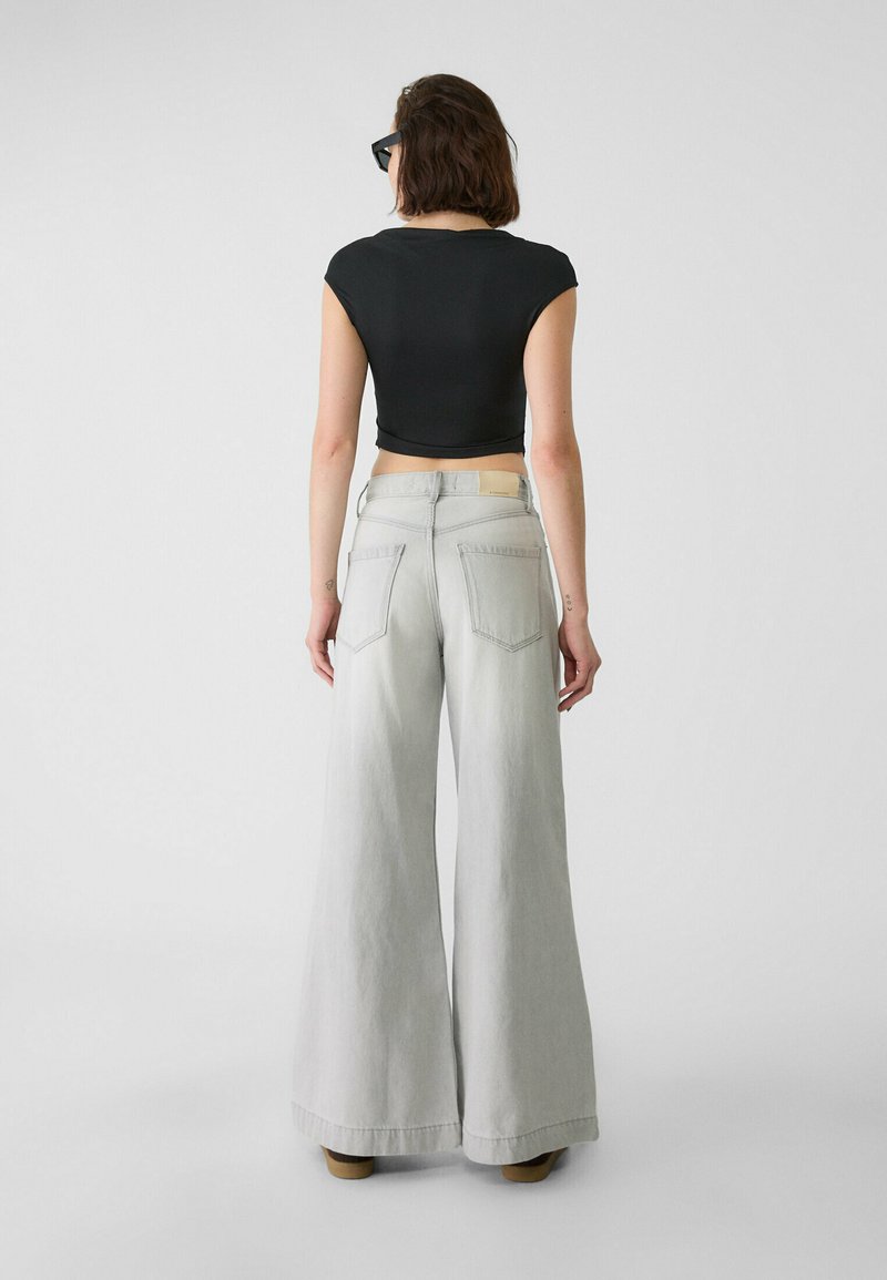 Jean large gris clair en denim, comportant deux poches arrière et une taille haute. Assorti à un haut noir ajusté et court.