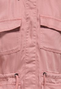 Różowa, lekka kurtka z tkaniny, z przednim zamkiem błyskawicznym, dwoma kieszeniami na piersi, regulowanym sznurkiem w talii oraz subtelną fakturą i gładkim wykończeniem.