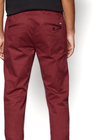 Chinos in cotone bordeaux con tasche posteriori, dettagli con bottoni e una texture liscia, caratterizzati da una vestibilità slim e un design minimal.