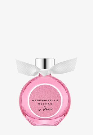 Flacon de parfum rond rose avec bouchon argenté et nœud blanc, étiqueté "Mademoiselle Rochas à Paris" sur un fond rose pailleté.