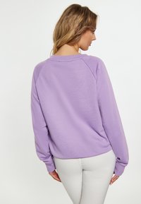 Pullover lungo a maniche lunghe di colore viola chiaro con un fit rilassato, maniche raglan e scollatura a coste. Tessuto morbido con una finitura liscia sul retro.