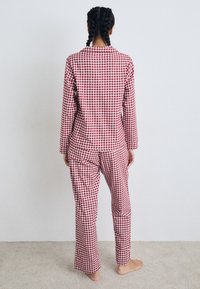 Rød og hvid ternet pyjamassæt med lange ærmer og lige bukser, lavet af blødt stof, set fra ryggen.