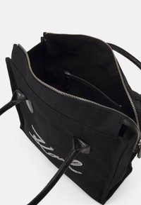 Black fabric tote bag with leather accents, zip closure, and internal pocket. Features a decorative silver text design on the front.