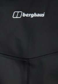 Svart sportkläder med en mjuk textur, prydd med vit "berghaus"-logotyp längs toppen. Sömmar i nederkant.