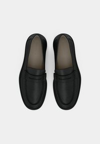 Mocassins en cuir noir à texture lisse, bout arrondi, surpiqûres décoratives et couture surélevée le long du bord supérieur.