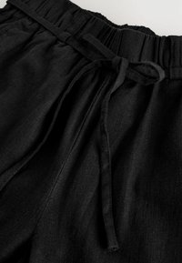 Fekete vászon rövidnadrág, elasztikus derékkal és húzózsinórral. Az anyag enyhén textúrált felülettel rendelkezik, és laza fazonú.