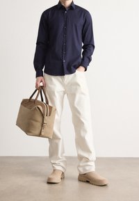 Marine knoop-overhemd, crèmekleurige broeken, beige tas met bruine accenten en lichtbeige schoenen. Glad materiaal en gestructureerd ontwerp.