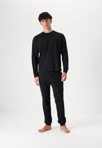 Sort langærmet bluse og bukser lavet af glat stof. Blusen har en rund halsudskæring, mens bukserne har elastiske manchetter ved anklerne.