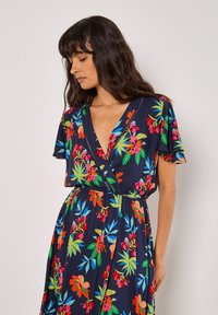 Robe portefeuille à motifs floraux avec un fond bleu marine, des motifs vibrants rouges, roses et verts, des manches courtes en volant et une taille élastique.