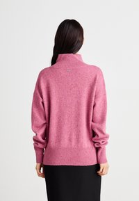 Pull à col roulé surdimensionné en tissu rose texturé, avec des poignets et un ourlet côtelés. Détail de logo discret à l'arrière.