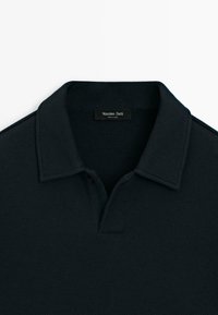 Mörkblå polo shirt i texturerad bomull, med klassisk krage, tvåknappsstängning och en vävd etikett inuti.