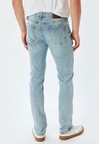 Jeans de mezclilla azul claro con corte recto, que presentan costuras en contraste, dos bolsillos traseros y un parche de cuero en la cintura.