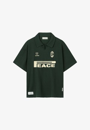 Mørkegrøn kortærmet polo med cremefarvet "PEACE"-tryk, to små logoer ovenover og krave med et hak i midten.