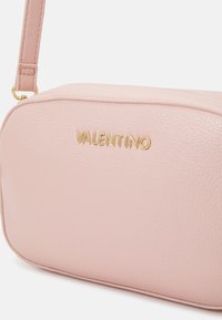Pink leather crossbody bag featuring a smooth texture, rounded shape, and gold embossed "VALENTINO" logo on the front. Adjustable strap.