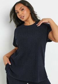 Tummansininen ribbed neulepaita lyhyillä hihoilla ja pyöreällä kaula-aukolla, jossa on rento istuvuus ja sivuhalkiot lisäämään liikkuvuutta.