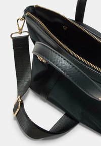 Borsa nera con esterno texturizzato, zip dorata e tracolla regolabile. L'interno è foderato in tessuto con una tasca con zip.