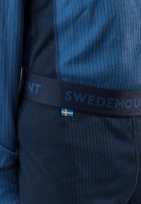 Close-up of blue ribbed long-sleeve top and bottom with a waistband showing "Swedemount" text and a small Swedish flag tag.
