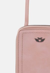 Rosa læder crossbody taske med lynlåslukning, som har en syet kant og et metallogo, der er formet som vinger og et hjerte.