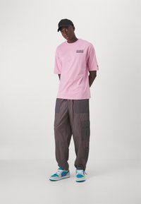 Camiseta de algodón rosa con el logo de "Los Angeles Dodgers", combinada con pantalones cargo grises con bolsillos de parche y zapatillas con toques azules.