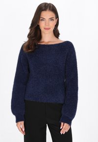 Granatowy, puszysty sweter z dzianiny z szerokim dekoltem w łódkę i d�ługimi, balonowymi rękawami. Tekstura materiału wydaje się miękka i ciepła. W zestawieniu z czarnymi spodniami.