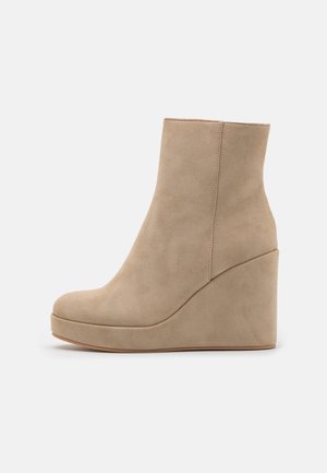 Bottine en daim beige avec talon compensé et bout arrondi, vue de côté sur fond blanc uni.
