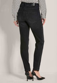 Vrouw in zwarte slim-fit jeans met kantafwerking bij de enkels en zwarte hoge hakken, gecombineerd met een gestreepte blouse met lange mouwen.