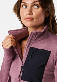 Lightweight purple polyester jacket with a zippered collar, textured fabric, and a black chest pocket featuring a logo and zip detail.