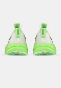 Chaussures de sport blanches avec des accents verts, tiges en tissu texturé, col rembourré et semelles épaisses en caoutchouc vert. Détails réfléchissants sur les talons.