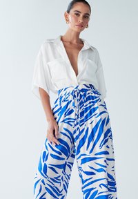 Chemise blanche à manches courtes, accompagnée d'un pantalon ample à rayures bleu et blanc avec une taille élastique.