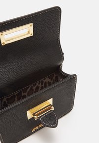 Svart läderhandväska med texturerad yta, guldhardwarelås och inredning i leopardmönster. Har kontrasterande vit sömnad.