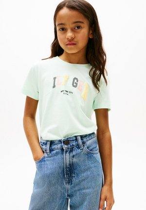 T-shirt in cotone verde chiaro con grafica "Hilfiger" in lettere multicolori, abbinata a jeans in denim a vita alta con chiusura a bottone.